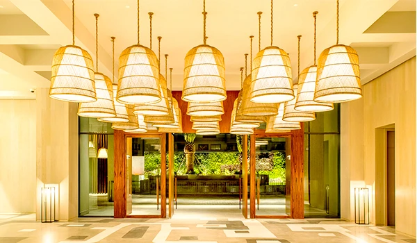 Imagem de uma entrada de um dos hotéis de luxo do Rio de Janeiro com iluminação suspensa elegante, paredes brancas, portas de madeira e grande janela de vidro com vista para jardim.