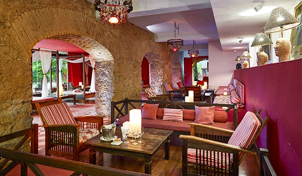 Interior de restaurante ou lounge com móveis de madeira, almofadas, paredes de pedra e iluminação aconchegante, ideal para momentos de lazer e socialização.