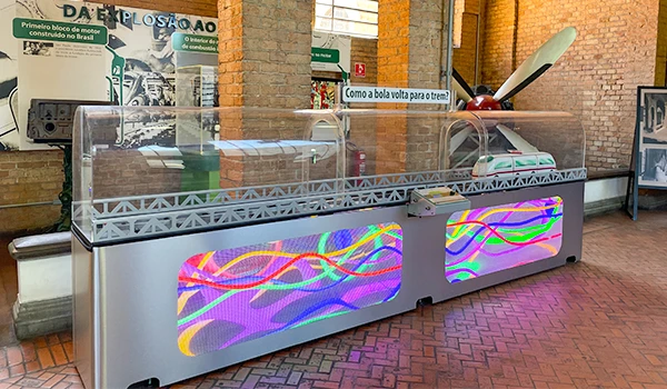 Exposição de um carro antigo em um museu ao lado de uma cabine de exibição com iluminação colorida na cidade de São Paulo, destacando a história do transporte.