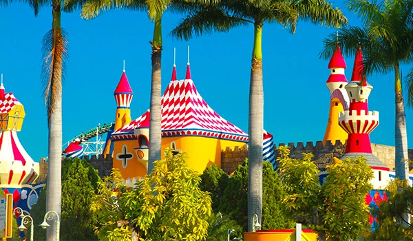 Castelo com telhados coloridos, uma das atrações do Hopi Hari, o parque temático com muitas palmeiras ao fundo, criando um cenário vibrante e divertido para visitantes de todas as idades.