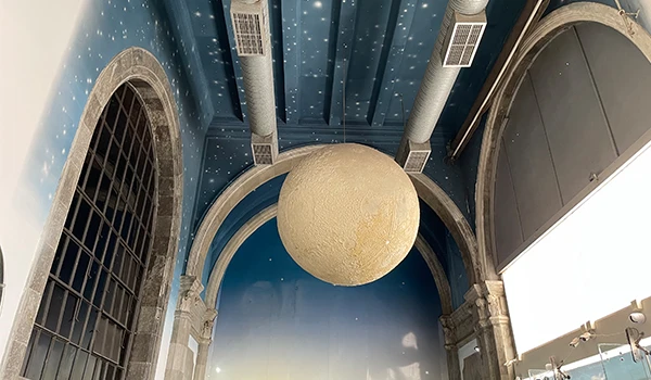 Imagem de um teto com decoração de estrelas, uma lua de papel pendurada, e detalhes arquitetônicos em um ambiente interno com céu estrelado.