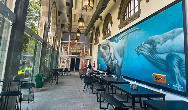 Imagem de um restaurante com decoração temática de oceanos e focas, mesas e cadeiras ao ar livre e parede com mural de animais marinhos, incluindo focas. Atrações do Museu Catavento.