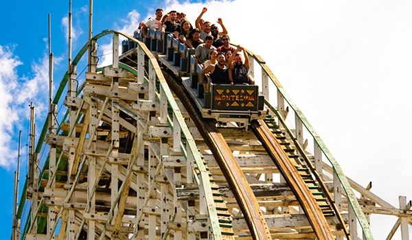 Grupo de pessoas se divertindo em uma emocionante montanha russa de madeira em um parque de diversões ao ar livre, aproveitando a adrenalina e a alegria nas atrações do Hopi Hari.