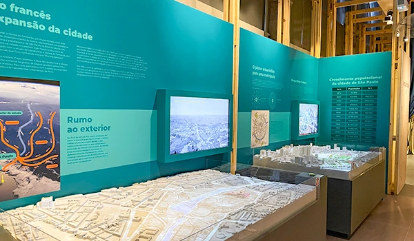 Exposição com painel informativo sobre a expansão da cidade de São Paulo e uma maquete detalhada do projeto urbano, destacando a infraestrutura e crescimento populacional na região.