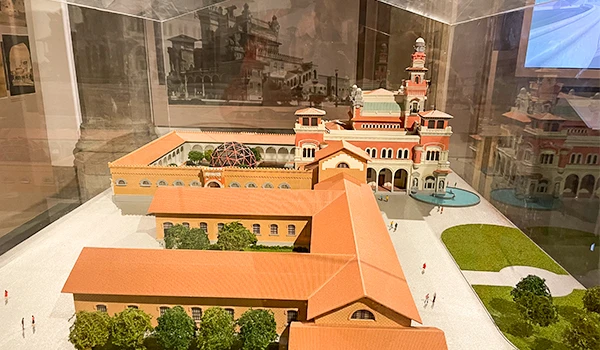 Modelo em escala de um palácio histórico com detalhes arquitetônicos e área verde ao redor, exibido em uma vitrine de museu.