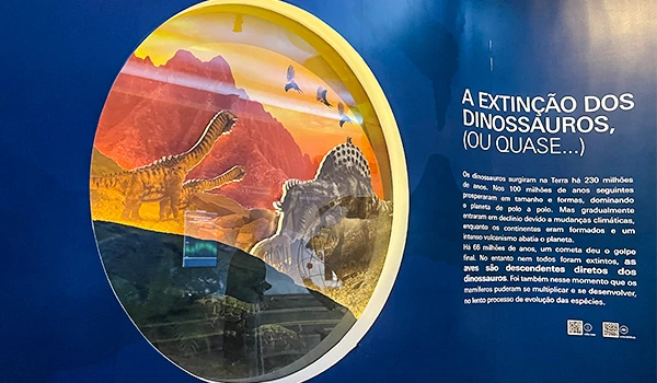 Exposição sobre a extinção dos dinossauros mostrando um painel ilustrativo com dinossauros famosos em um cenário de erupção vulcânica, destacando informações educativas. Ideal para quem busca aprender sobre a história da extinção dos dinossauros.