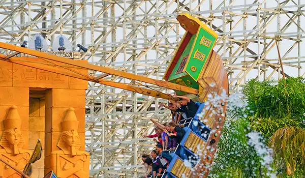 Diversão em um parque de diversões com montanha-russa e casais aproveitando o passeio ao ar livre, com estrutura de madeira e elementos decorativos vibrantes das atrações do Hopi Hari.