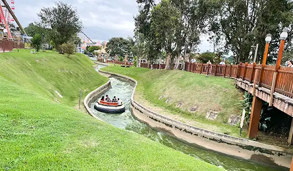 Pessoas no escorregador aquático em parque com muitas árvores e paisagem verde ao redor, em um dia ensolarado.