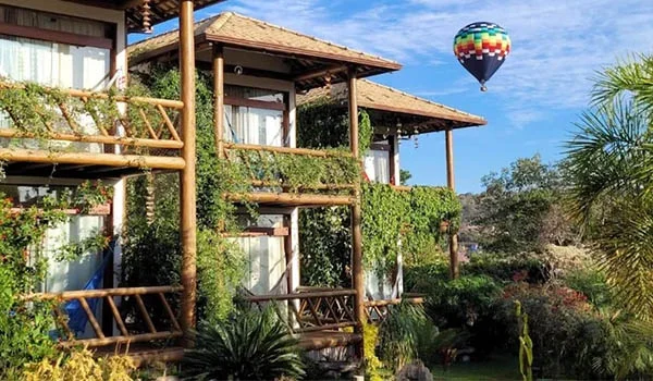 Foto de um hotel com varandas entre plantas e um balão no céu colorido. Lua de Mel América Latina.
