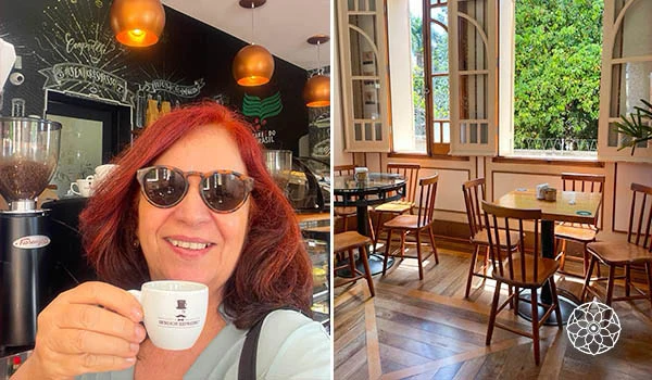 Deusa Rodrigues segurando uma xícara de café em um ambiente de cafeteria, ao lado de uma sala com mesas e cadeiras próximas a uma janela com vista para o jardim.