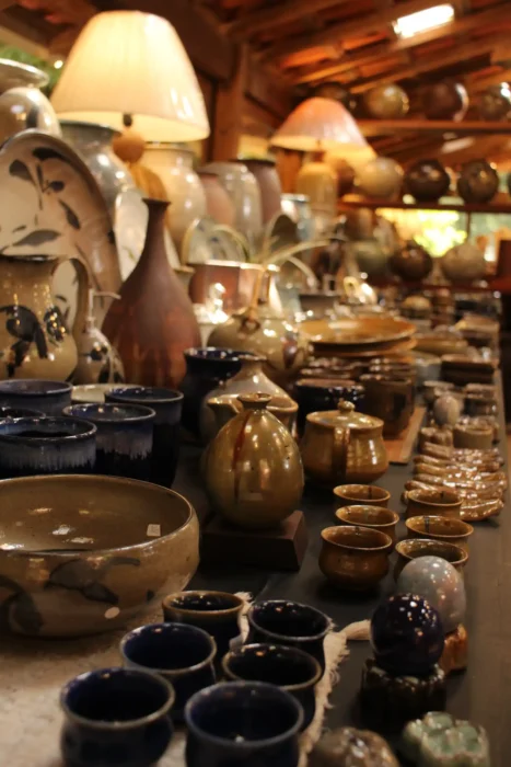 Ambiente de loja com cerâmicas e utensílios de cozinha artesanais em prateleiras e balcão, incluindo potes de cobre e tigelas de barro, sob iluminação quente. Cunha capital da cerâmica.
