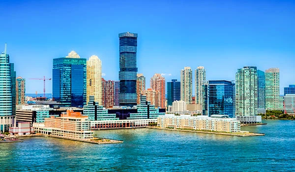 Vista panorâmica do skyline da cidade em dia ensolarado, com arranha-céus modernos ao longo de um rio e prédios refletindo no céu azul, com construção e infraestrutura urbana ao fundo. Cidades dos Estados Unidos na Copa.