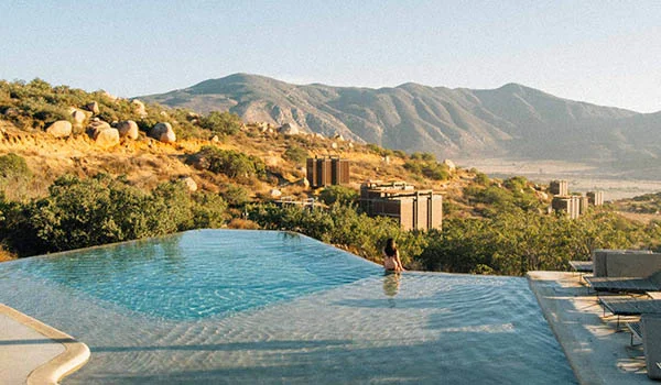 Foto de uma piscina com borda infinita em meio a uma paisagem de montanhas e prédios.