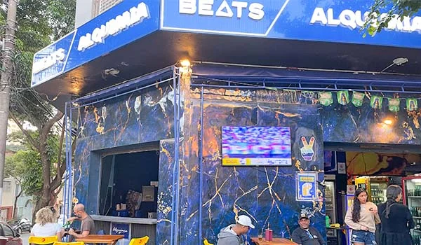 Foto do Alquimia Bar, com fachada e placa em tons de azul com vários clientes nas mesas na calçada, uma das coisas legais para fazer na Barra Funda.