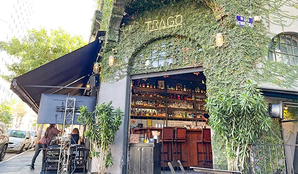 Foto da fachada do bar Trago, que fica em frente do Bar Estrago, com a fachada coberta de vegetais e mesas na calçada. Um dos lugares com coisas legais para fazer na Barra Funda.