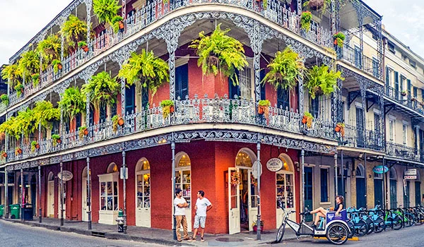 Foto da French Quarter em New Orleans, um predinho histórico colorido, cercado de samambaias e com turistas e bicicletário à frente.