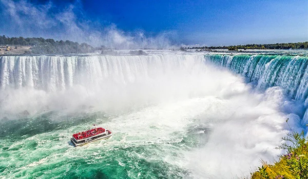 Foto das Cataratas de Niagra, com grande volume de água e um barco com passeio de turistas nos Estados Unidos.