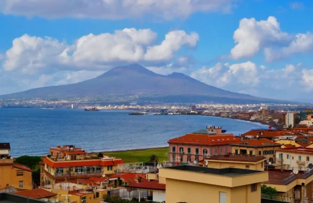 Imagem da cidade de Nápoles com construções histórica, o mar e ao fundo o Vulcao Vesúvio na Itália.
