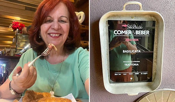 Deusa Rodrigues segura um garfo com comida diante de um prato; ao lado, uma placa emoldurada anuncia que o restaurante Basilicata foi finalista na categoria Trattoria do prêmio Comer & Beber São Paulo 2023/2024.