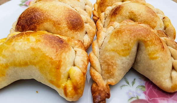 Empanadas assadas, douradas e recheadas, dispostas em um prato branco decorado com flores.