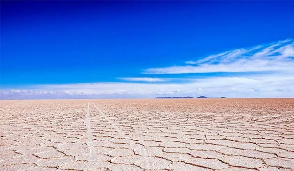 Salar de Uyuni, na Bolívia, com uma vasta planície de sal rachado, horizonte plano, céu azul intenso e nuvens brancas ao fundo. Pontos turísticos da Bolívia.