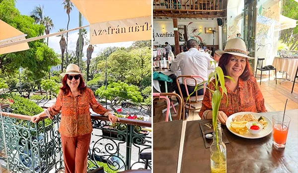 Mulher usando chapéu bege, óculos escuros, blusa estampada em tons de laranja e calça marrom em um restaurante chamado Azafrán. Na imagem à esquerda, ela posa em uma varanda com grades ornamentadas, cercada por árvores e palmeiras. À direita, está sentada à mesa durante uma refeição, com pratos de comida, um copo de suco e um pequeno vaso com planta. O ambiente é acolhedor, com decoração rústica, mesas de madeira e grandes janelas com vista para a área externa.