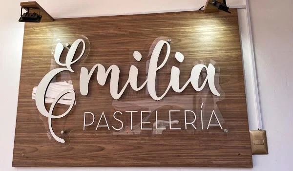 Placa de madeira com iluminação embutida e letras brancas exibindo o nome “Emilia Pastelería”.