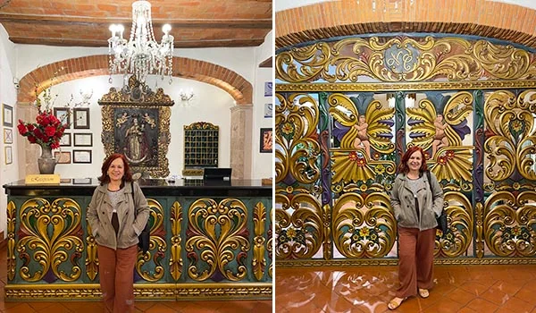 Deusa Rodrigues posando em duas áreas de um ambiente histórico, com paredes e arcos de tijolos aparentes, piso de cerâmica e decoração colonial. À esquerda, ela está diante de um balcão ornamentado em verde e dourado, sob um lustre de cristal e próximo a um altar com imagens religiosas. À direita, posa em frente a um grande painel decorativo com entalhes e motivos florais dourados, verdes e azuis. Ela veste jaqueta cinza, blusa clara e calça marrom.